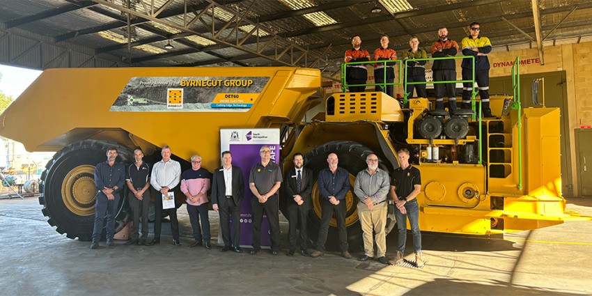 A group of people standing in front of a large yellow mining truck inside a warehouse