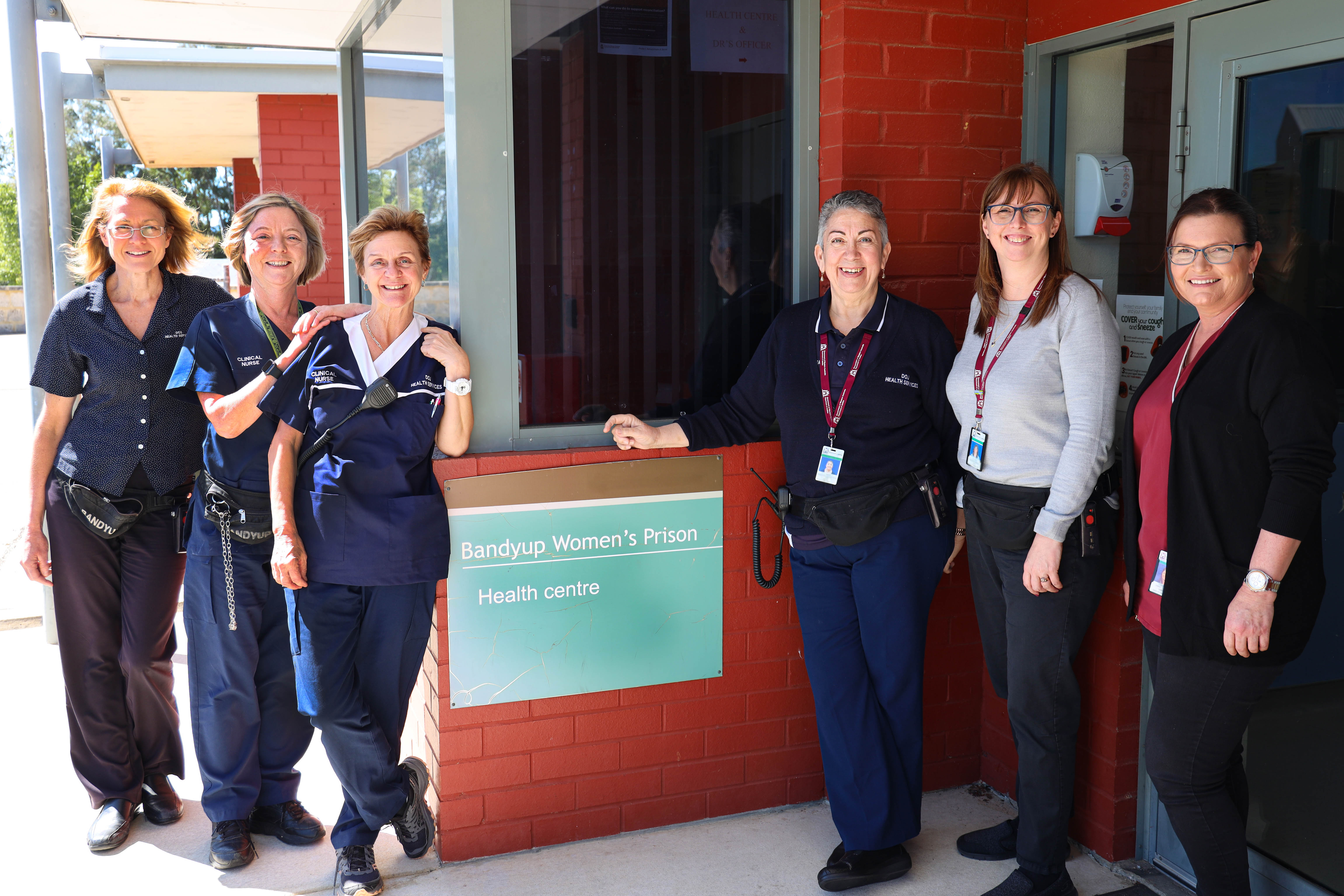 a group of female nurses and doctors stand around a green sign.