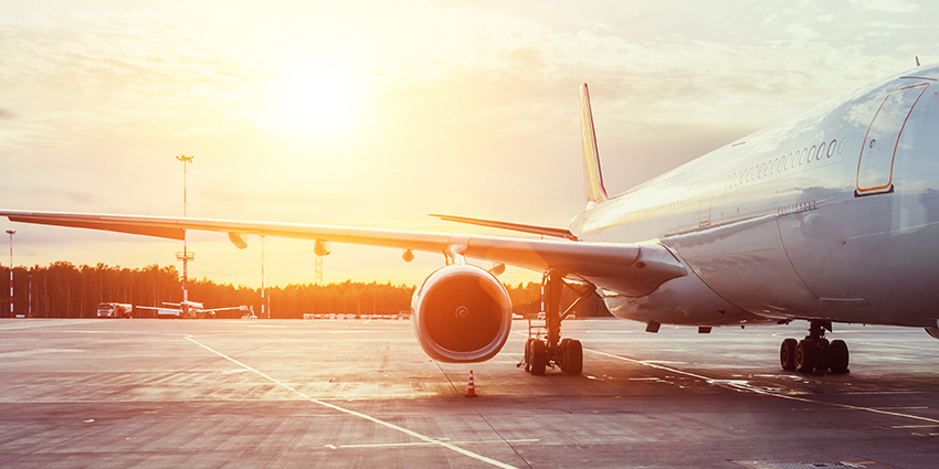 An airplane on the runway at an airport with a sunrise behind it