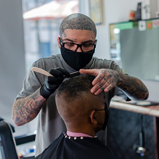 A barber wearing a mask giving a man a haircut.