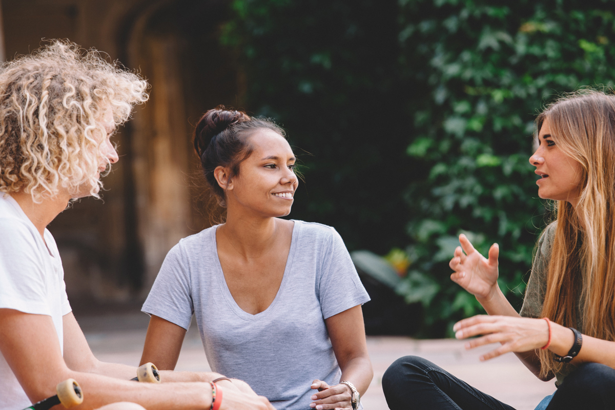 Image of three young adult women sitting in a garden setting having a conversation 