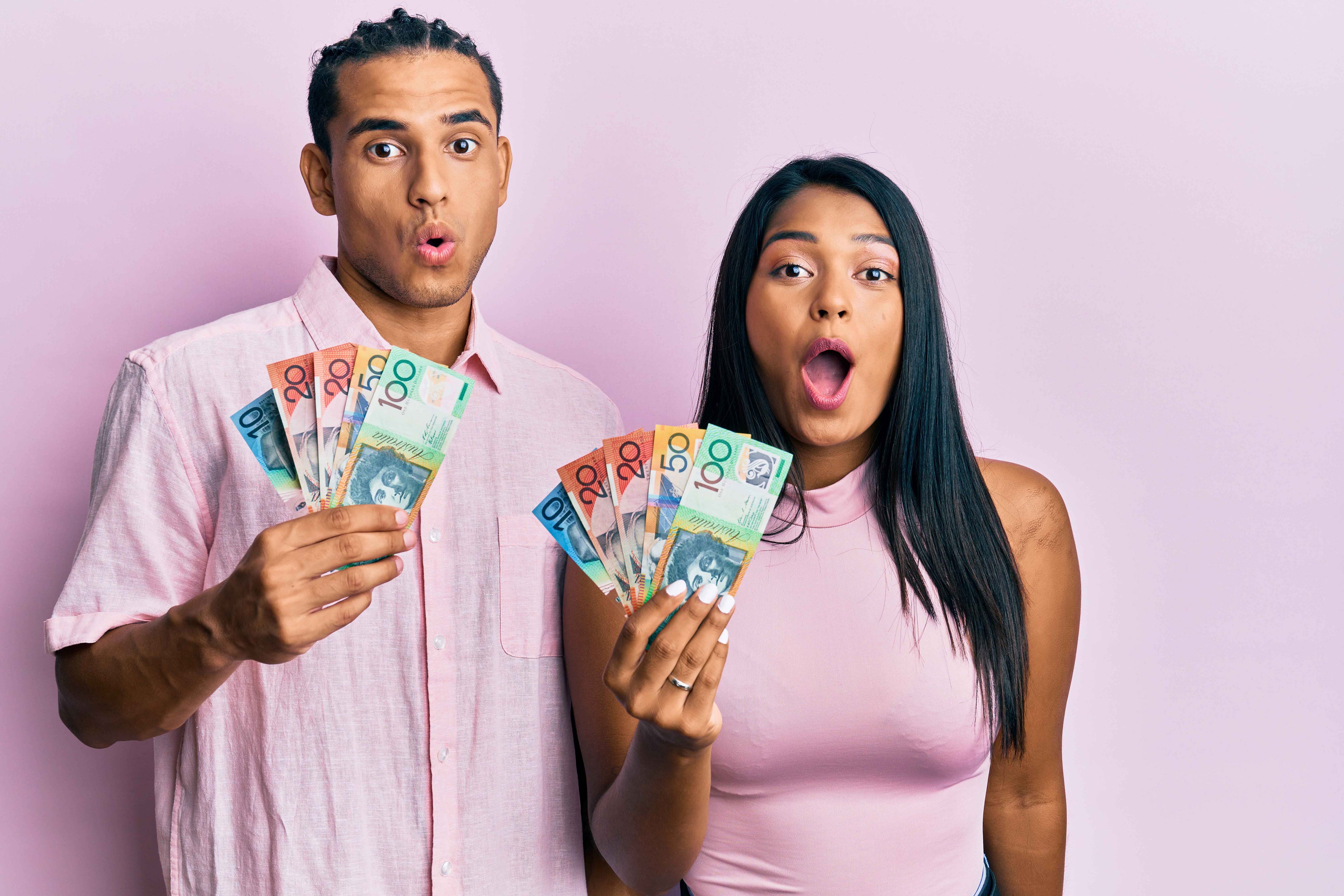 Young couple holding Australian dollars scared and amazed with open mouth for surprise, disbelief face