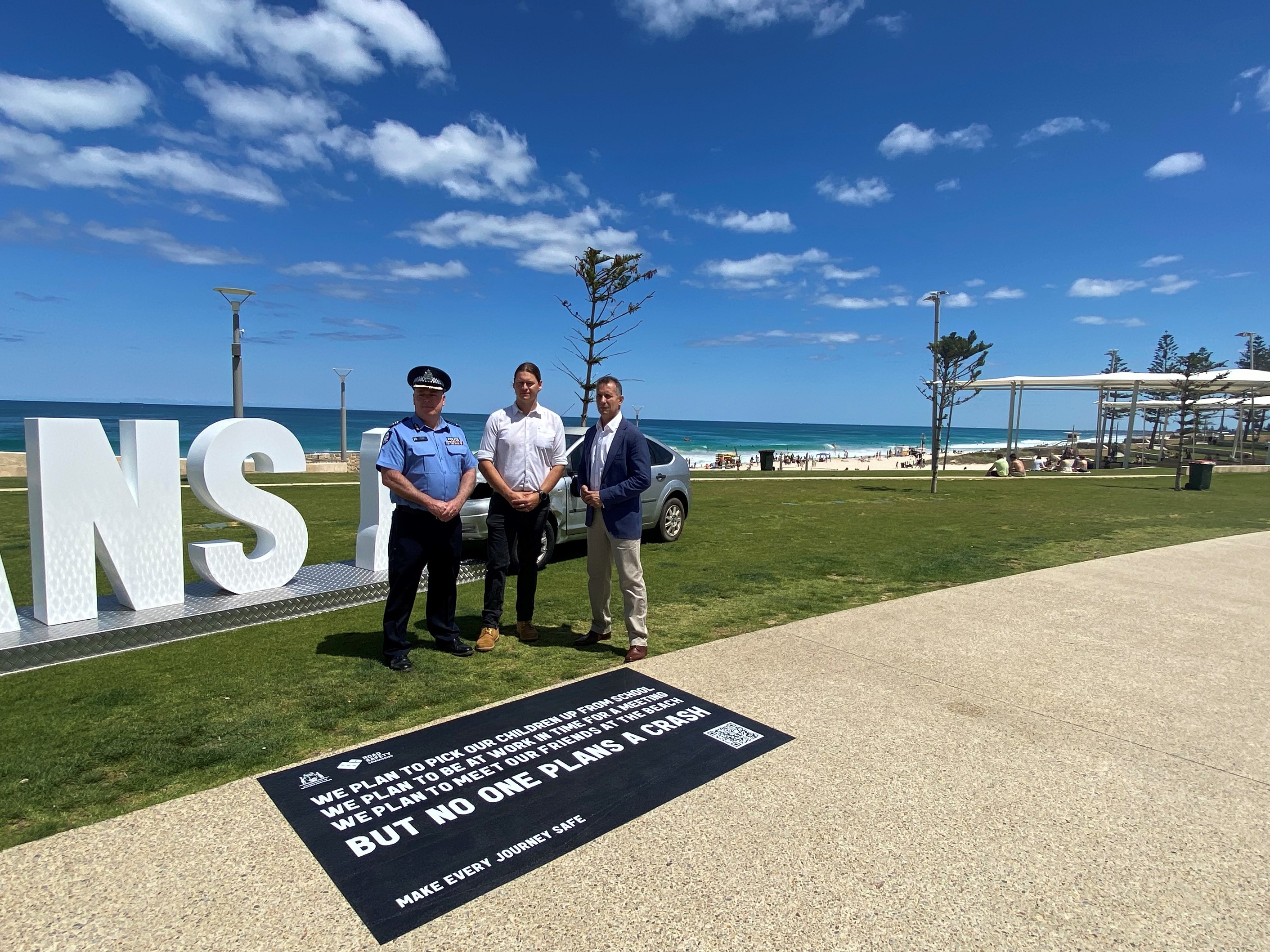 three people standing in front of an art installation made up of the words 'no one plans a' and a crushed vehicle