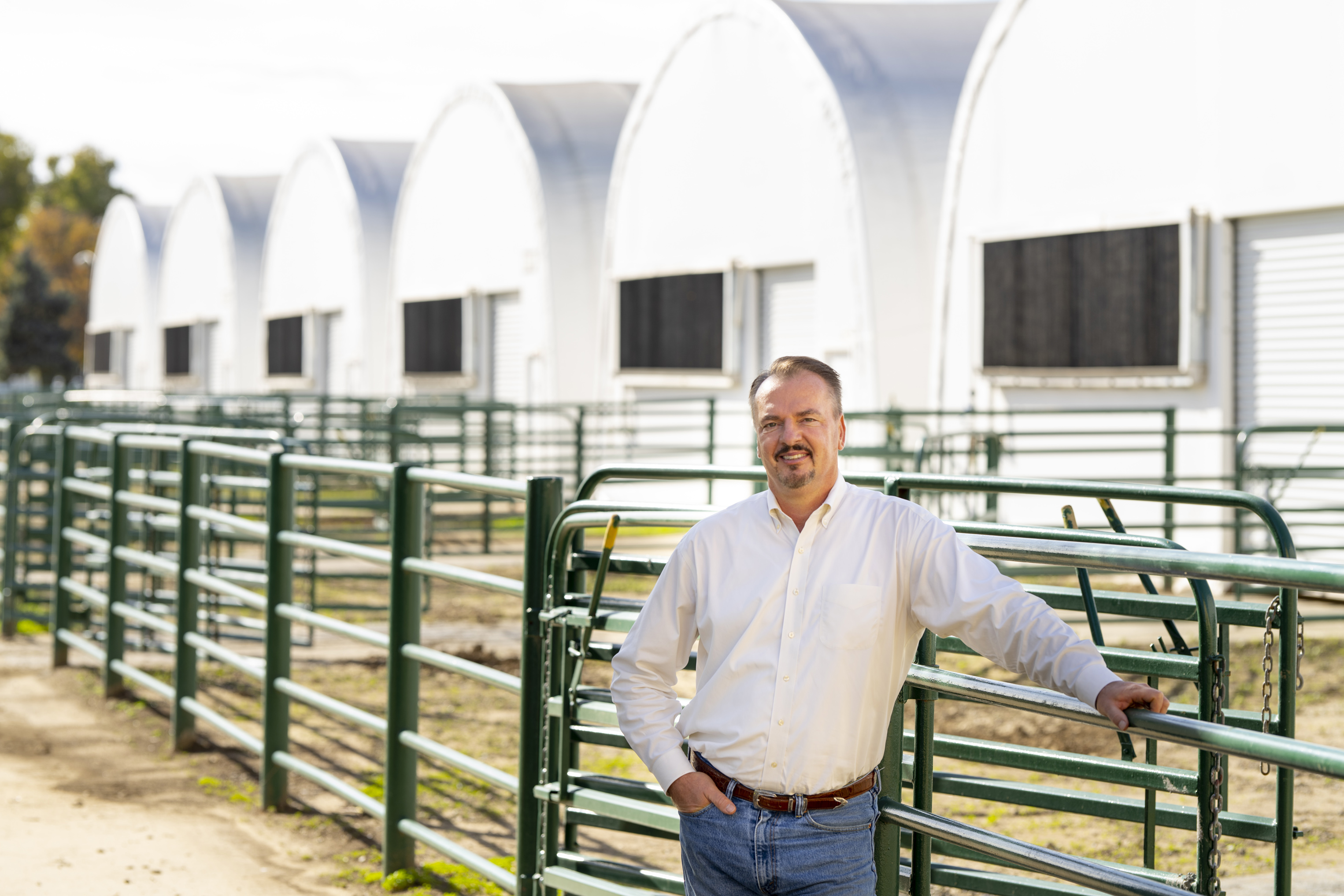 Publicity shot of Prof. Frank Mitloehner on farm property. Fences and barns in background.