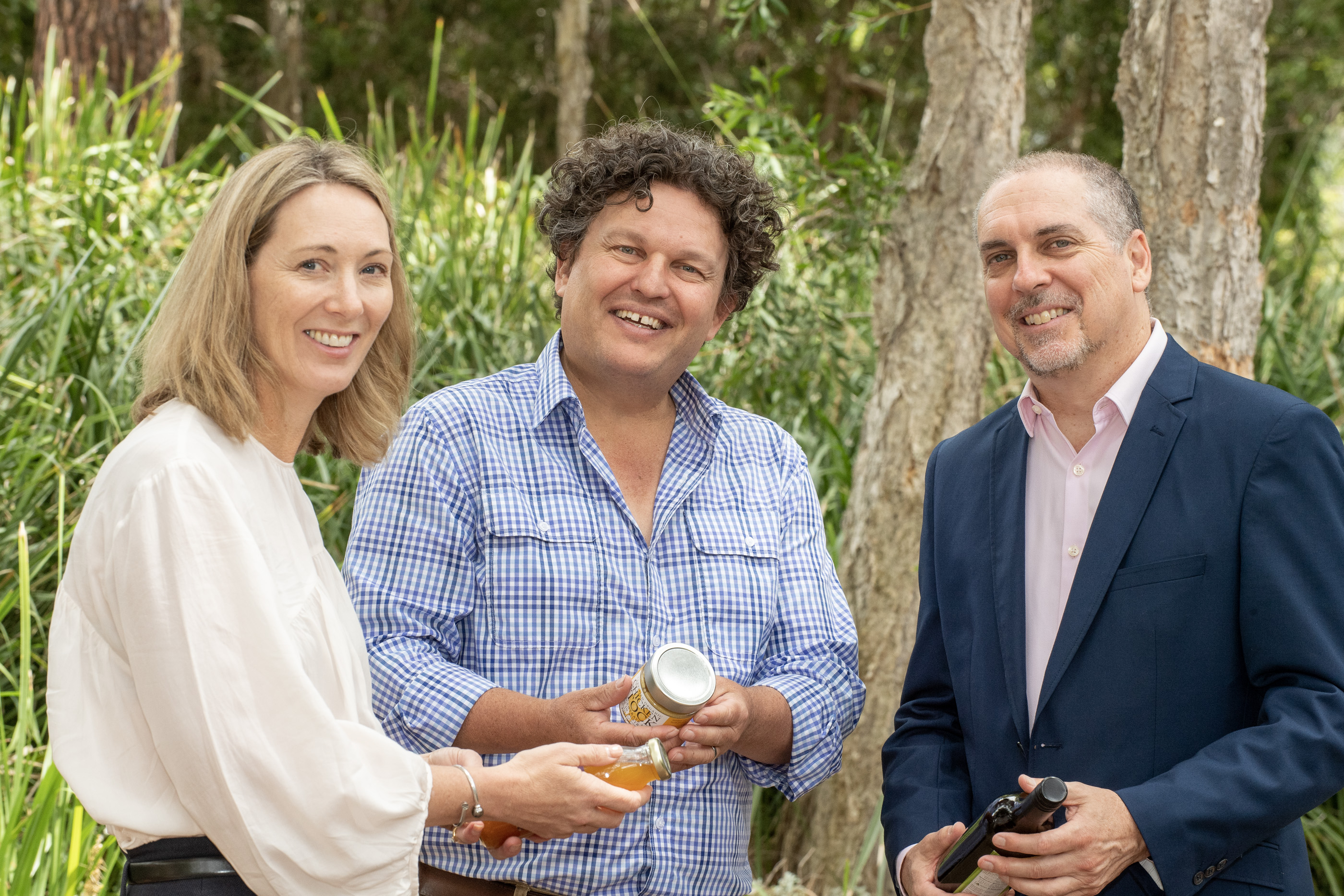 DPIRD business development manager Tamatha Newsome, Curtin University Dean of Sustainable Futures Professor Josh Bryne and industry and economic development manager Kim Antonio in outdoor setting holding food products.