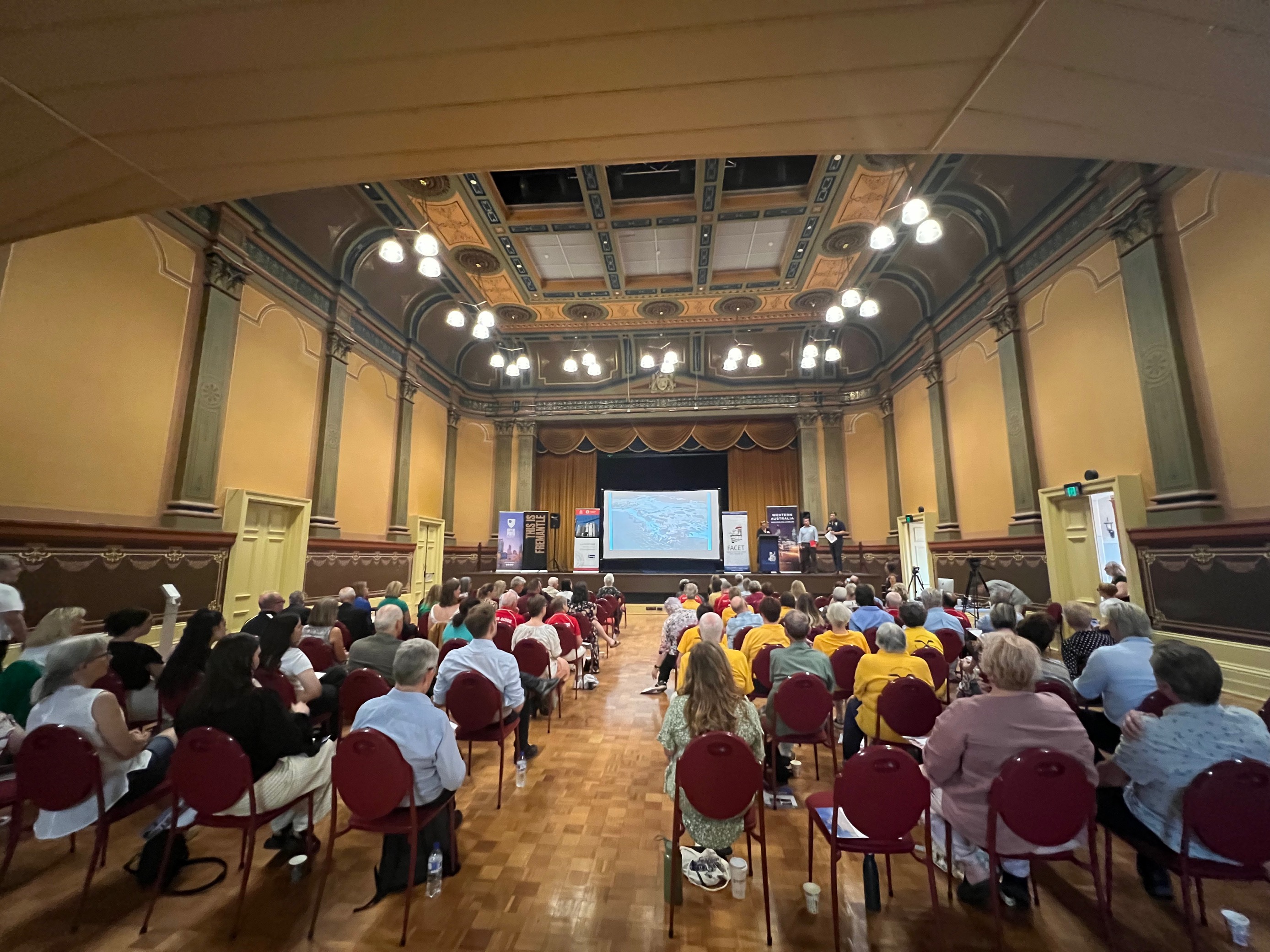 Photograph - people sitting down looking at presenters on a podium