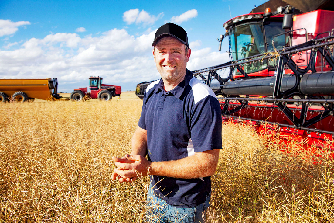 Mt Walker farmer Peter Cowan in field, grain harvesters in background