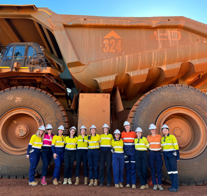 A group of women standing in front of a truck at a mine site 