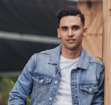 A portrait of Josh Bonesso in a denim jacket leaning on a wall