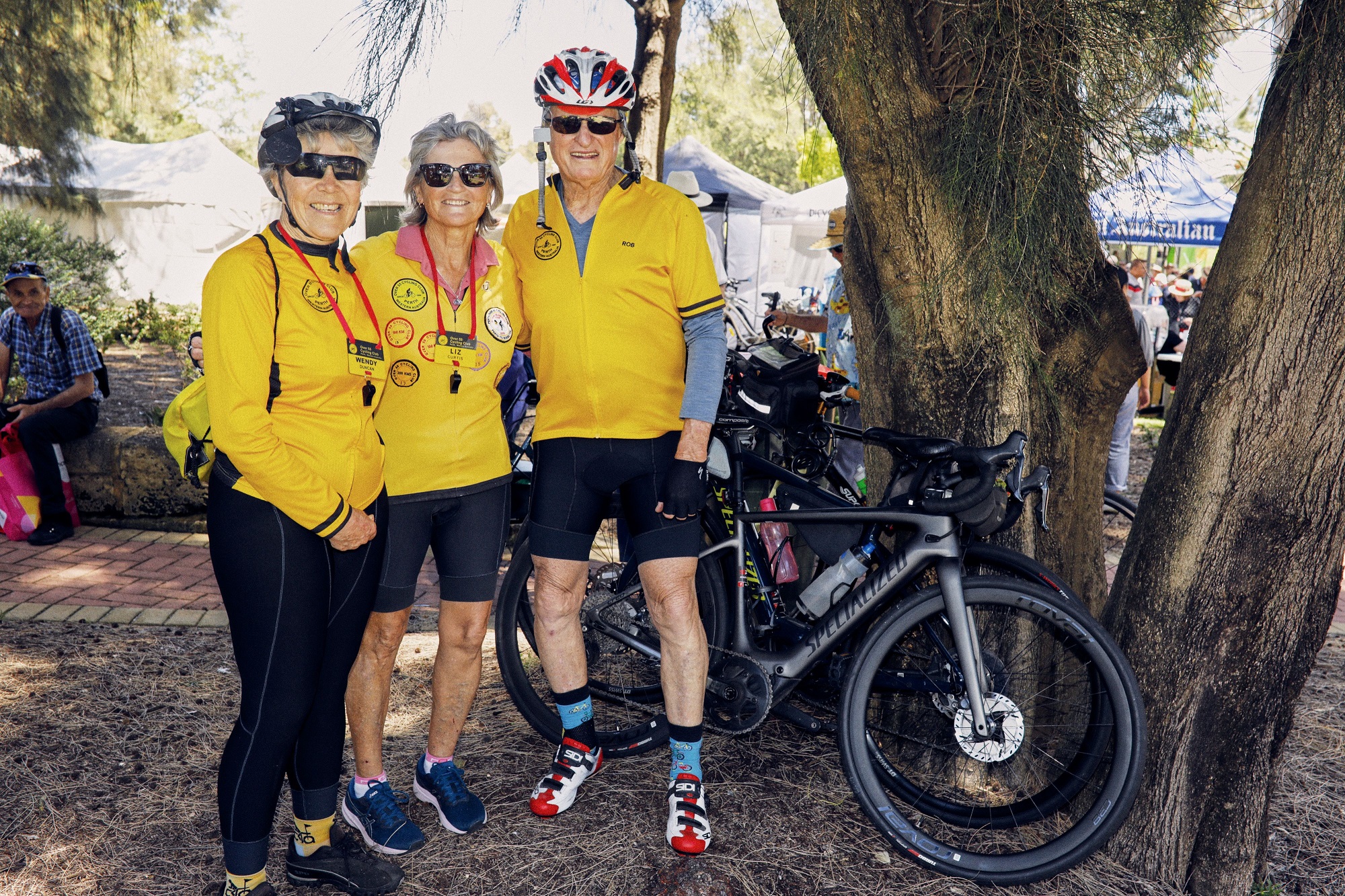 photo of three over 55 seniors in biking clothes, helmets and with their bikes