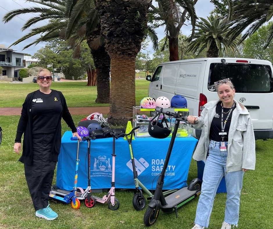 An image of two people posing in front of eRideable devices and a table containing bike helmets