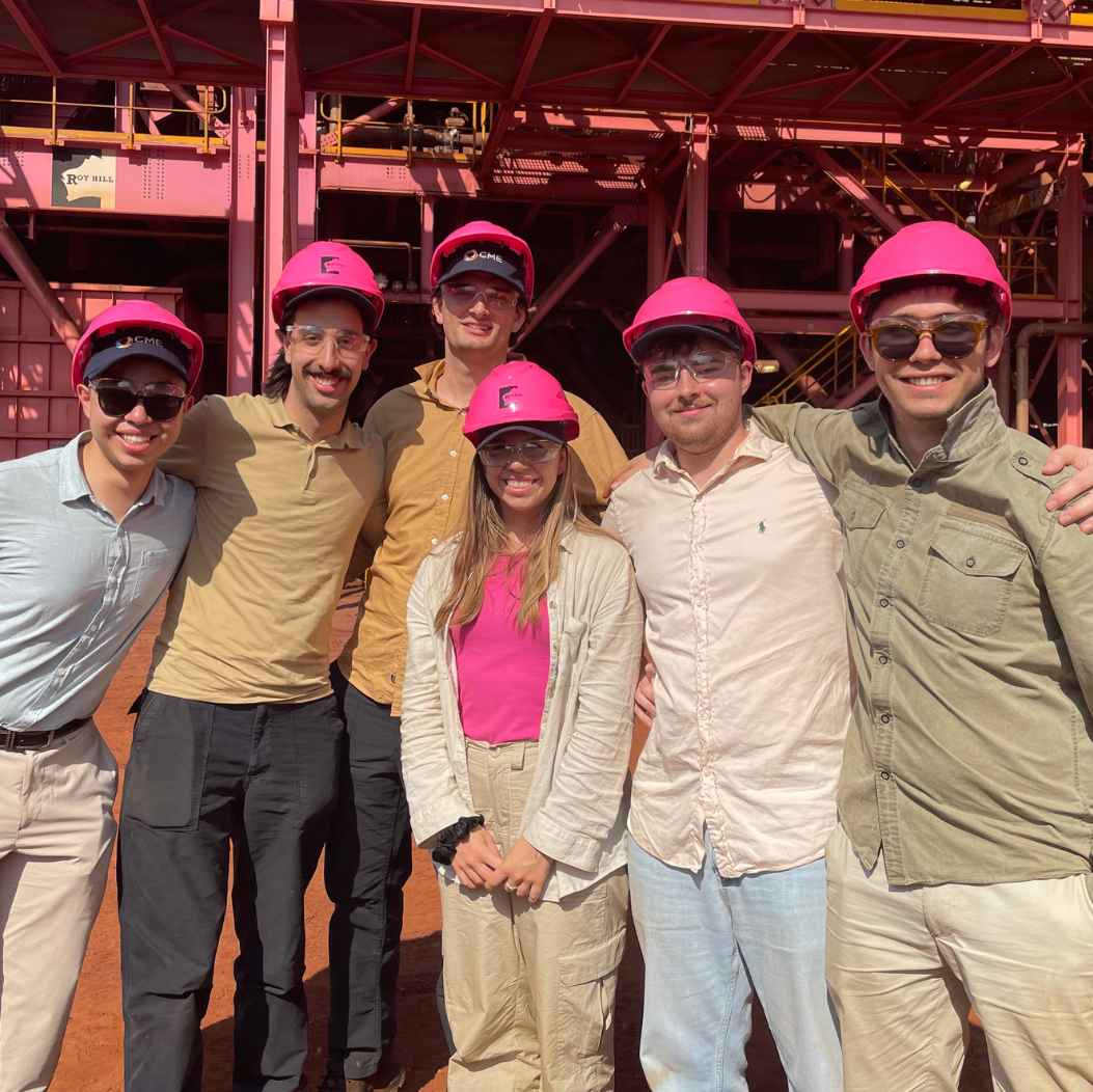A group of graduates with their arms around each other. They are all wearing pink hard hats. 