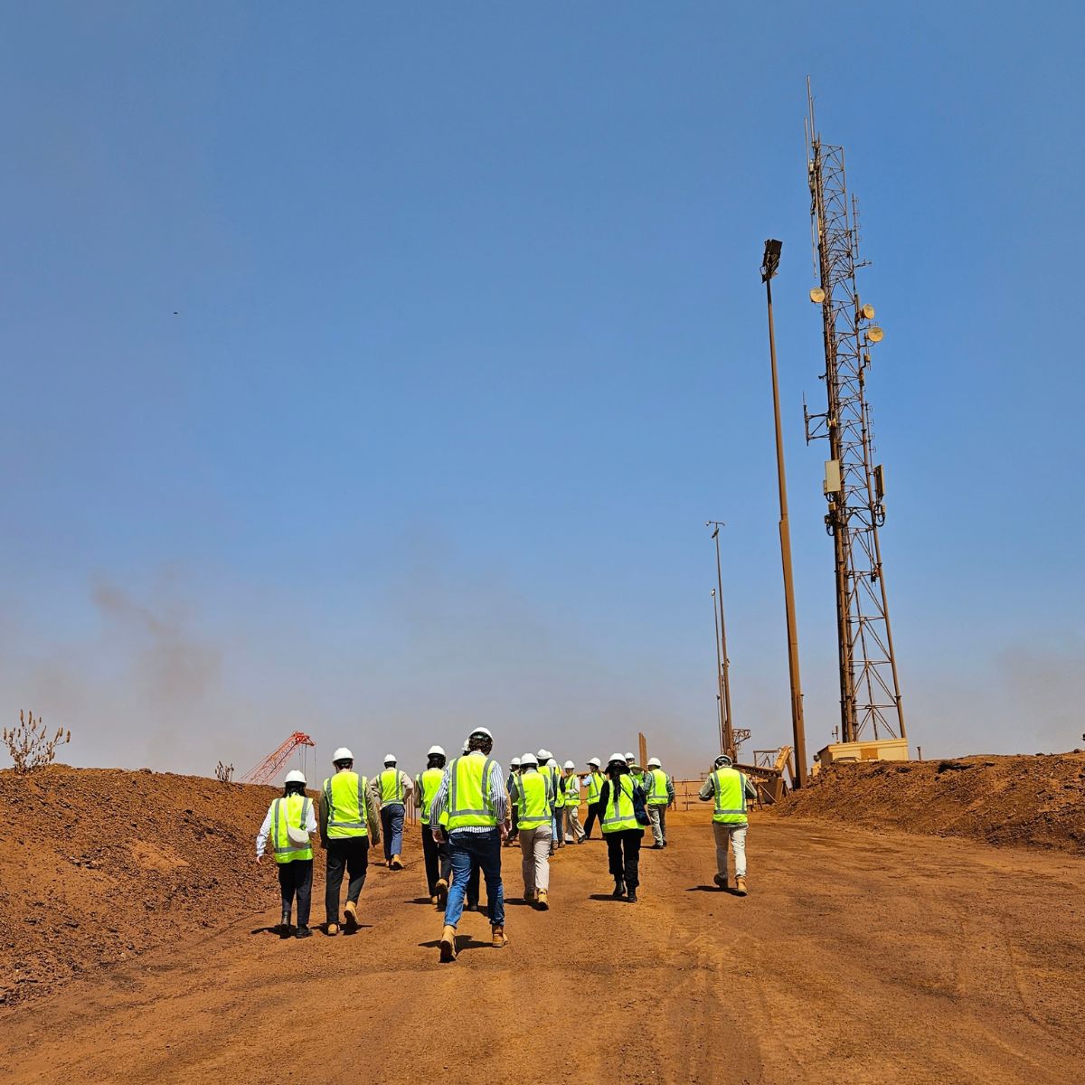A group of graduates walking down a red pilbara dirt path. The graduates yellow highvis vests contrast against the blue sky and red dirt.