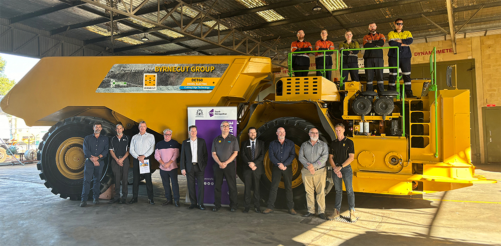 A group of people standing in front of a large yellow mining truck inside a warehouse