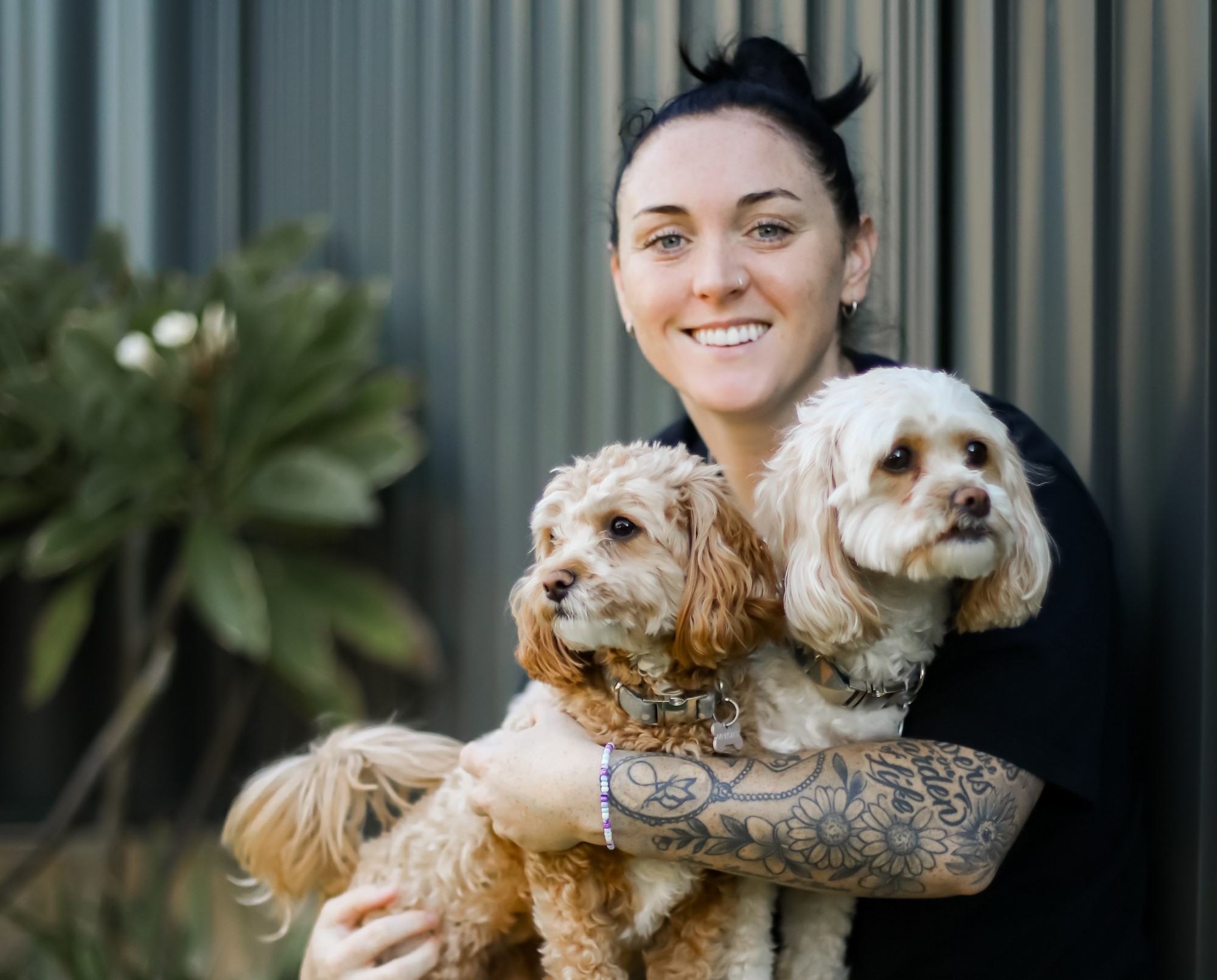 Image of a young adult woman smiling and hugging two pet dogs