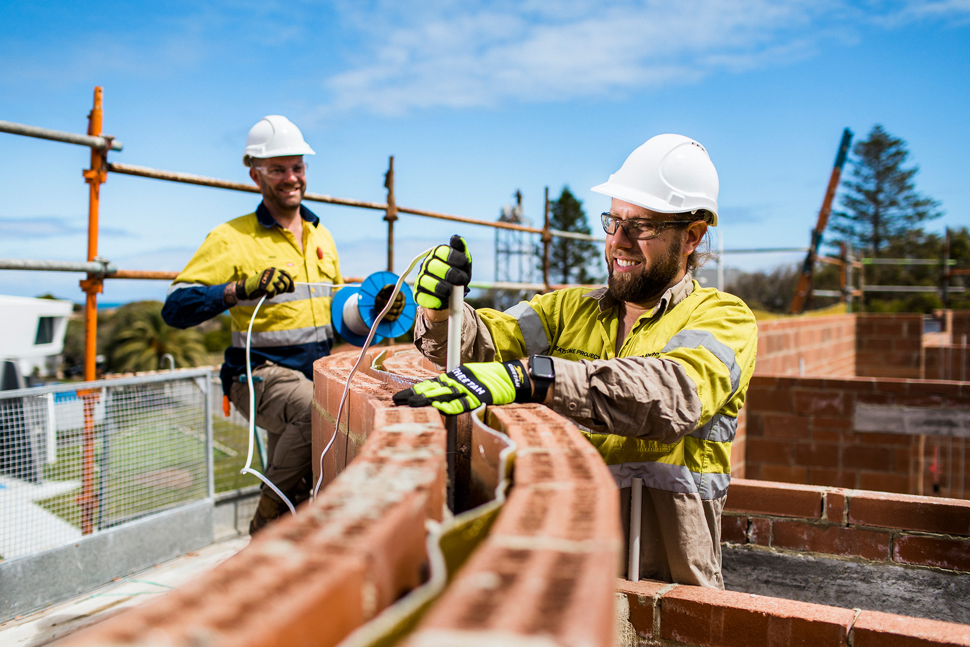 Two male construction workers, working outdoors, building a brick wall. 