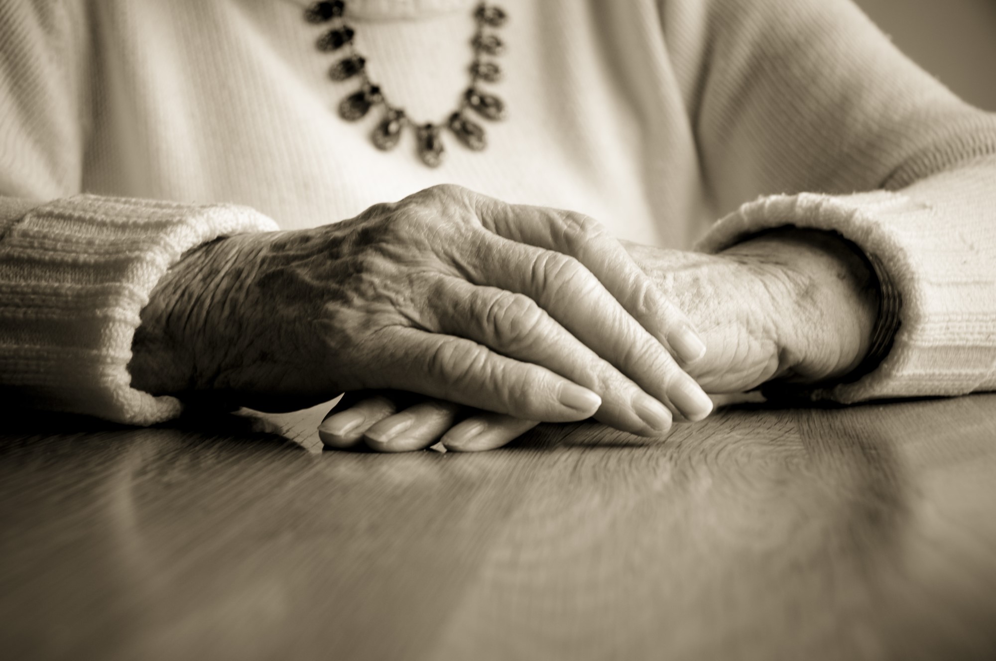 photo of an older woman sitting at a table with her hand placed over her other hand 