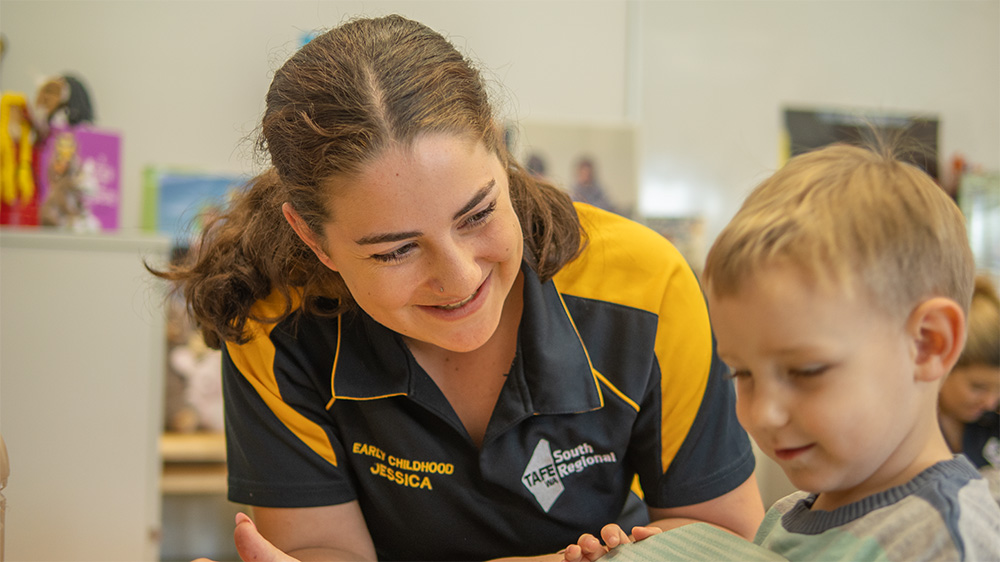An early childhood student, reading a book with a young boy at daycare.