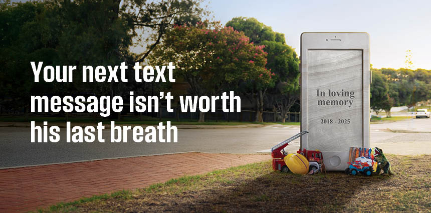 A young boy's headstone in the shape of a phone with the text "In Loving Memory" and toys around it.