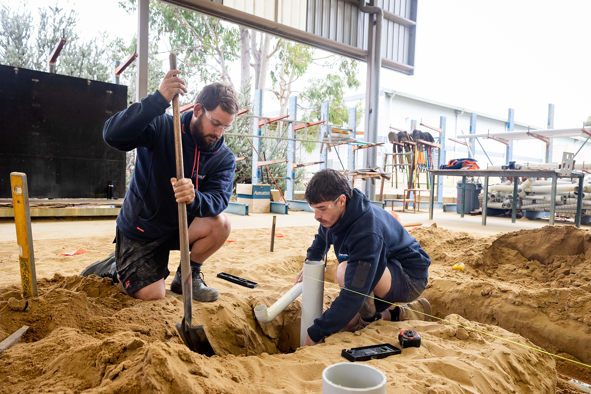 Two men using shovels to work in the sand, engaged in a collaborative effort outdoors.