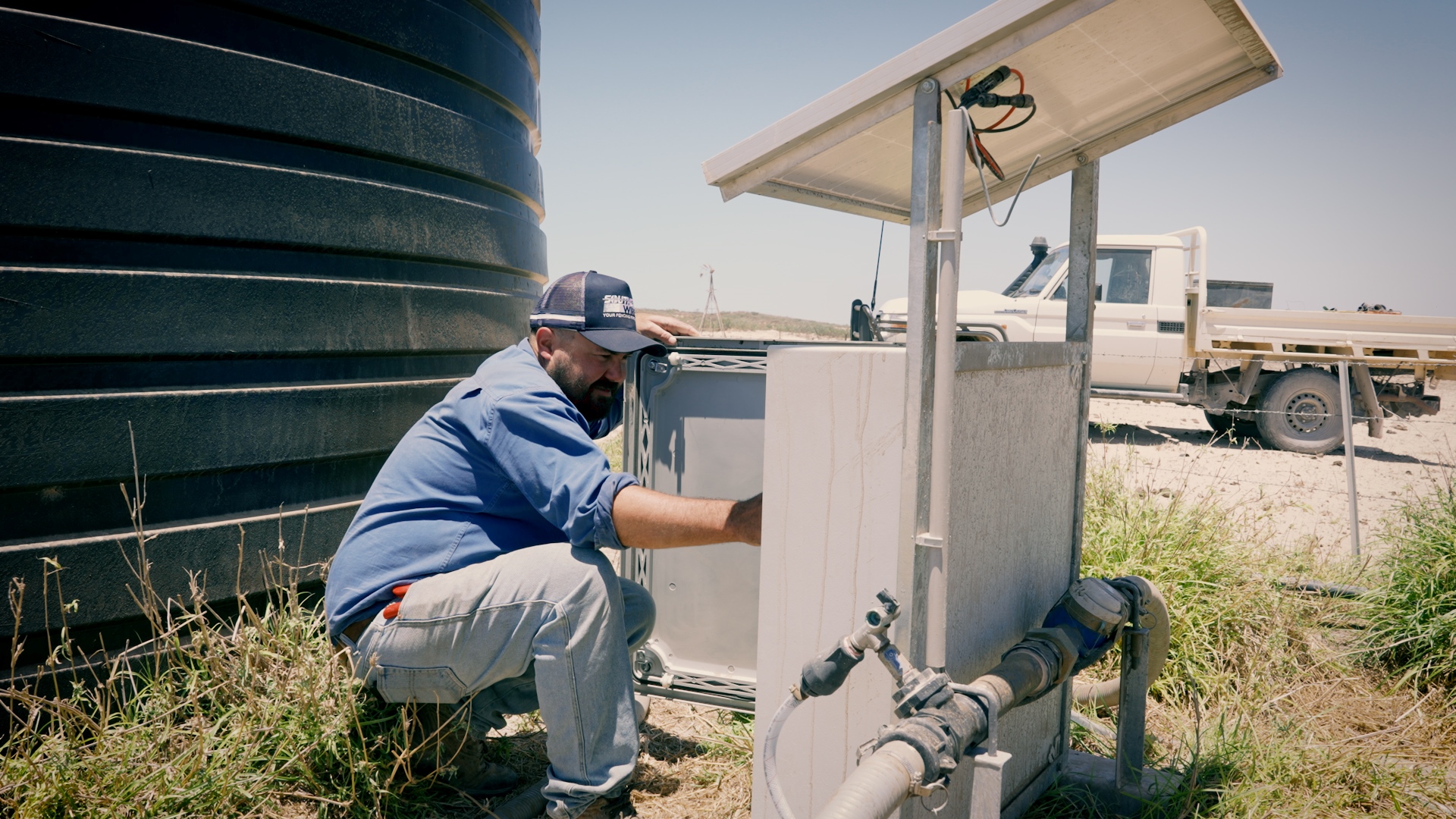 A man squatting near a box and a tank.