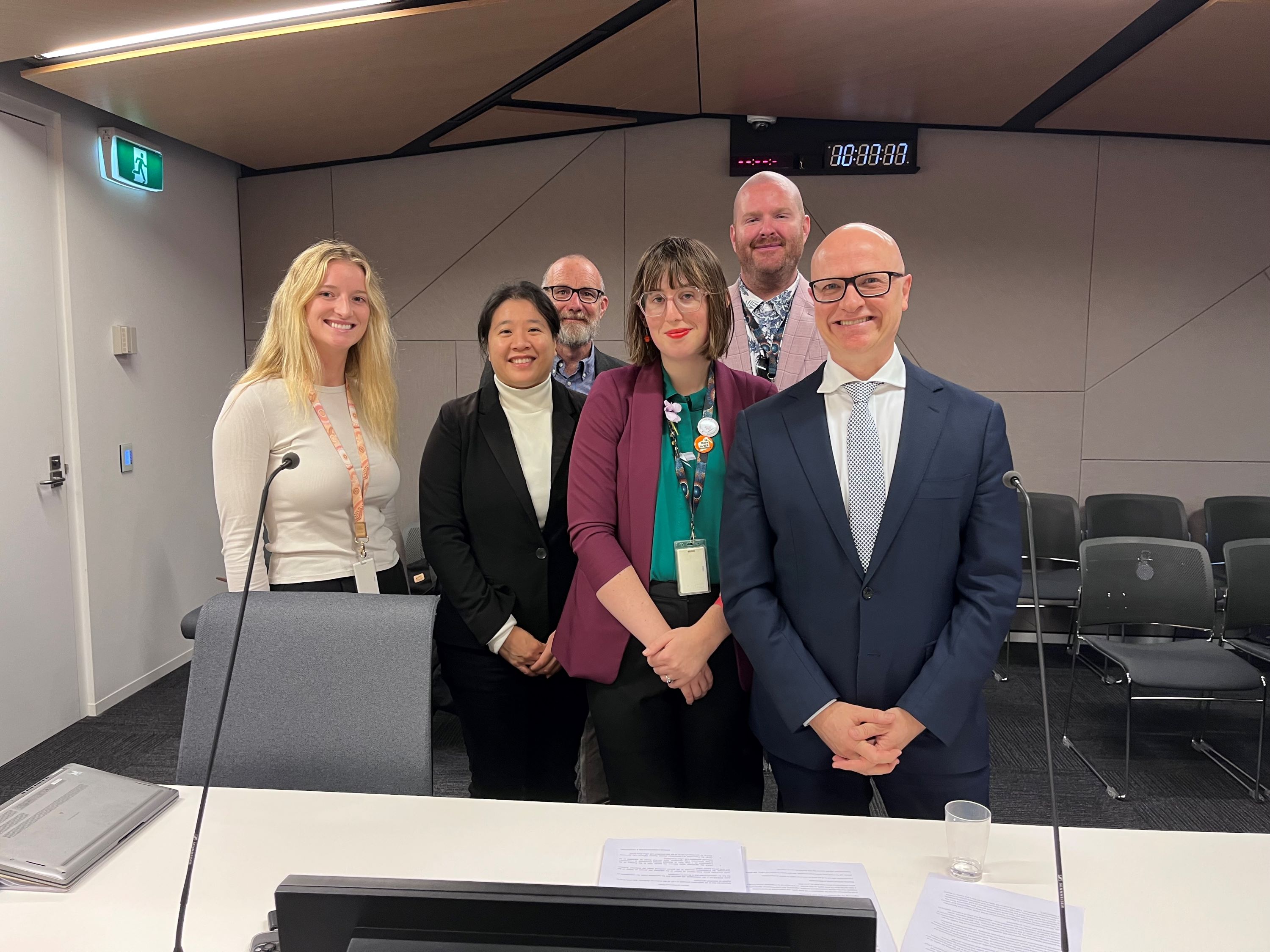 Photo of a group of Communities staff members including Director General Mike Rowe, photographed in a legal hearing room setting