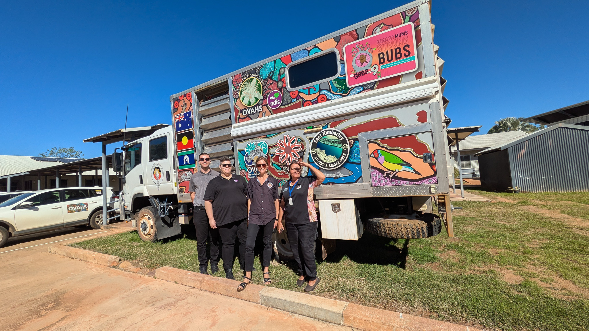 Four Working with Children Check Screening Unit workers standing in front of a brightly decorated truck. 