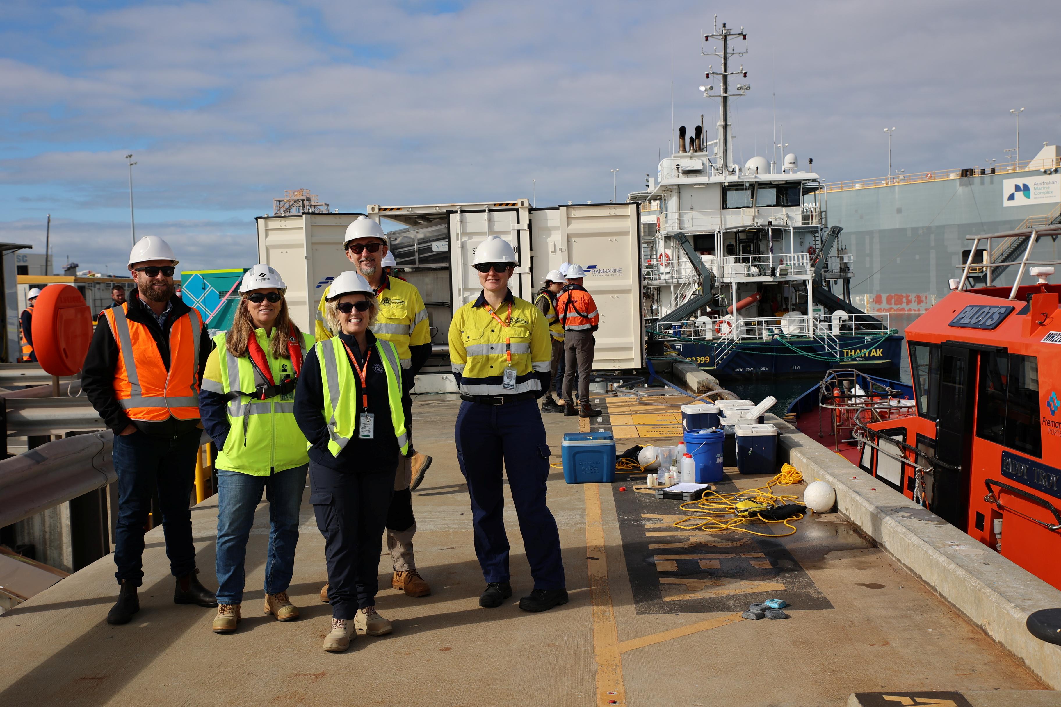 A group of people wearing hats and high-vis clothing on a wharf.