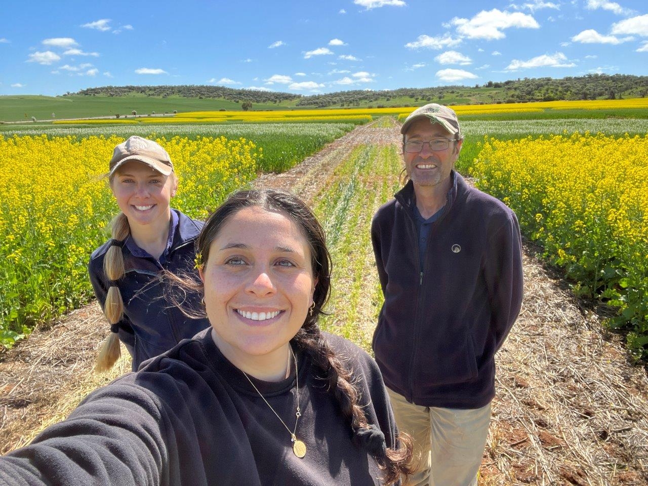 A man and two women in a canola paddock on a sunny day.