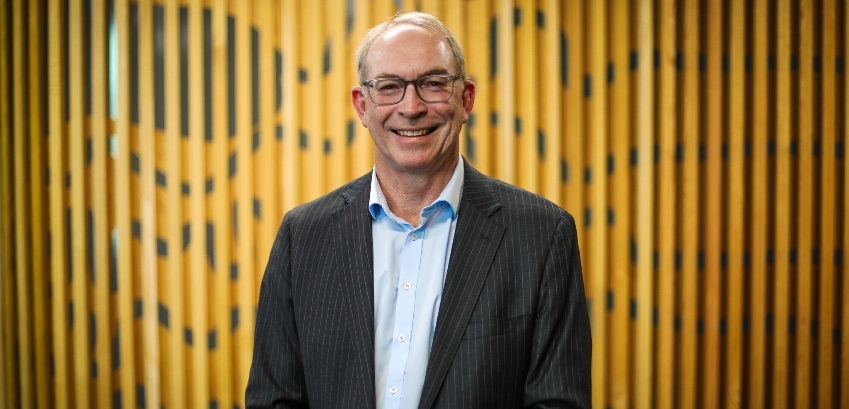 Photo of a middle age man formally dressed and smiling, in an indoor work environment