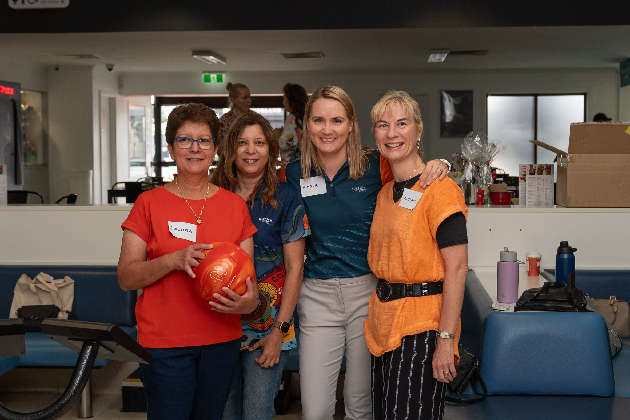 Photo of a group of four women wearing colourful clothing and smiling, in a casual indoor setting
