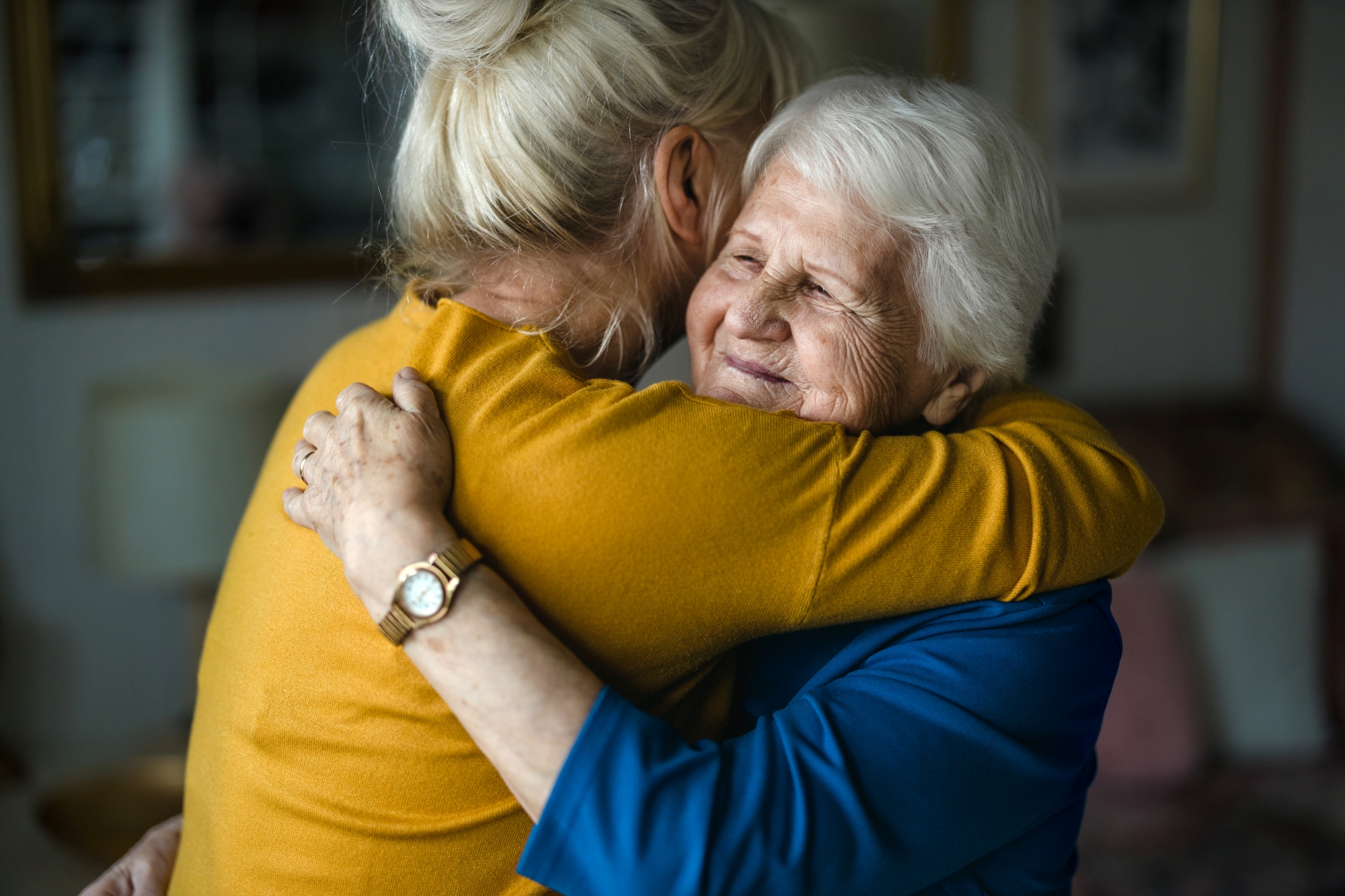 Two woman pictured in a hugging embrace, as if to comfort each other