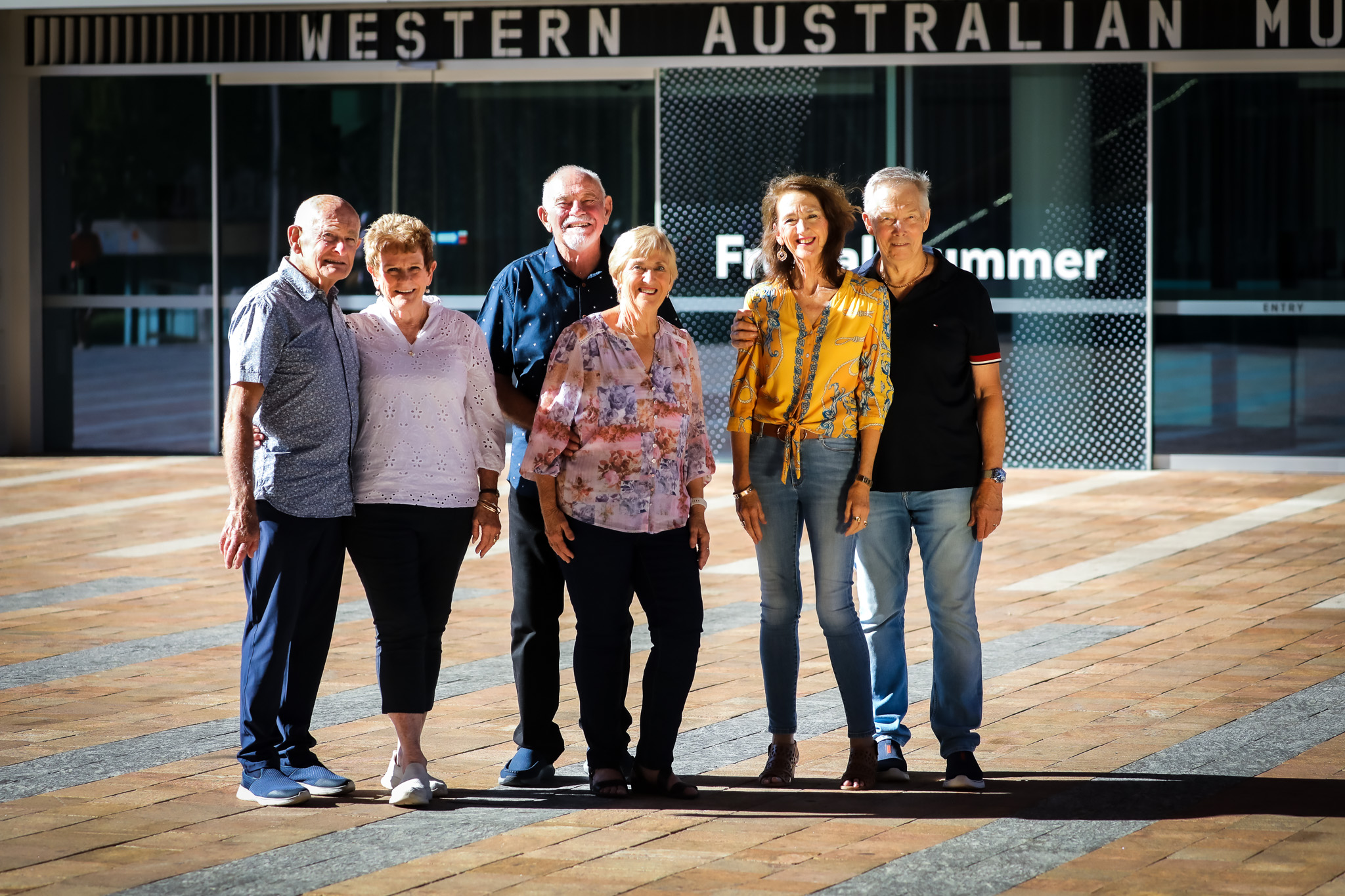 Six seniors standing outside the Western Australian Museum on a sunny day.