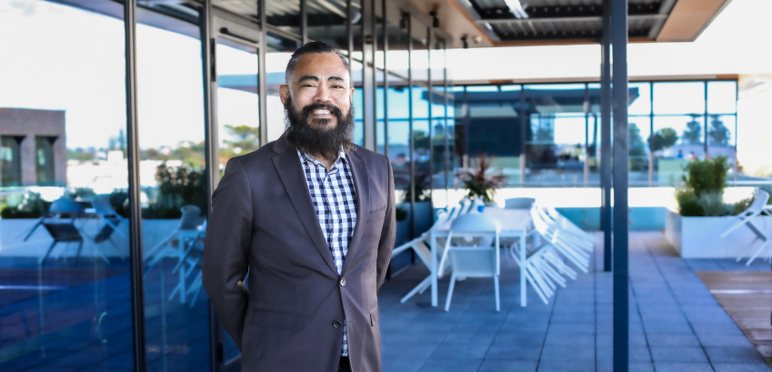 Photograph of a man smiling to camera, in an outdoor setting, wearing a suit