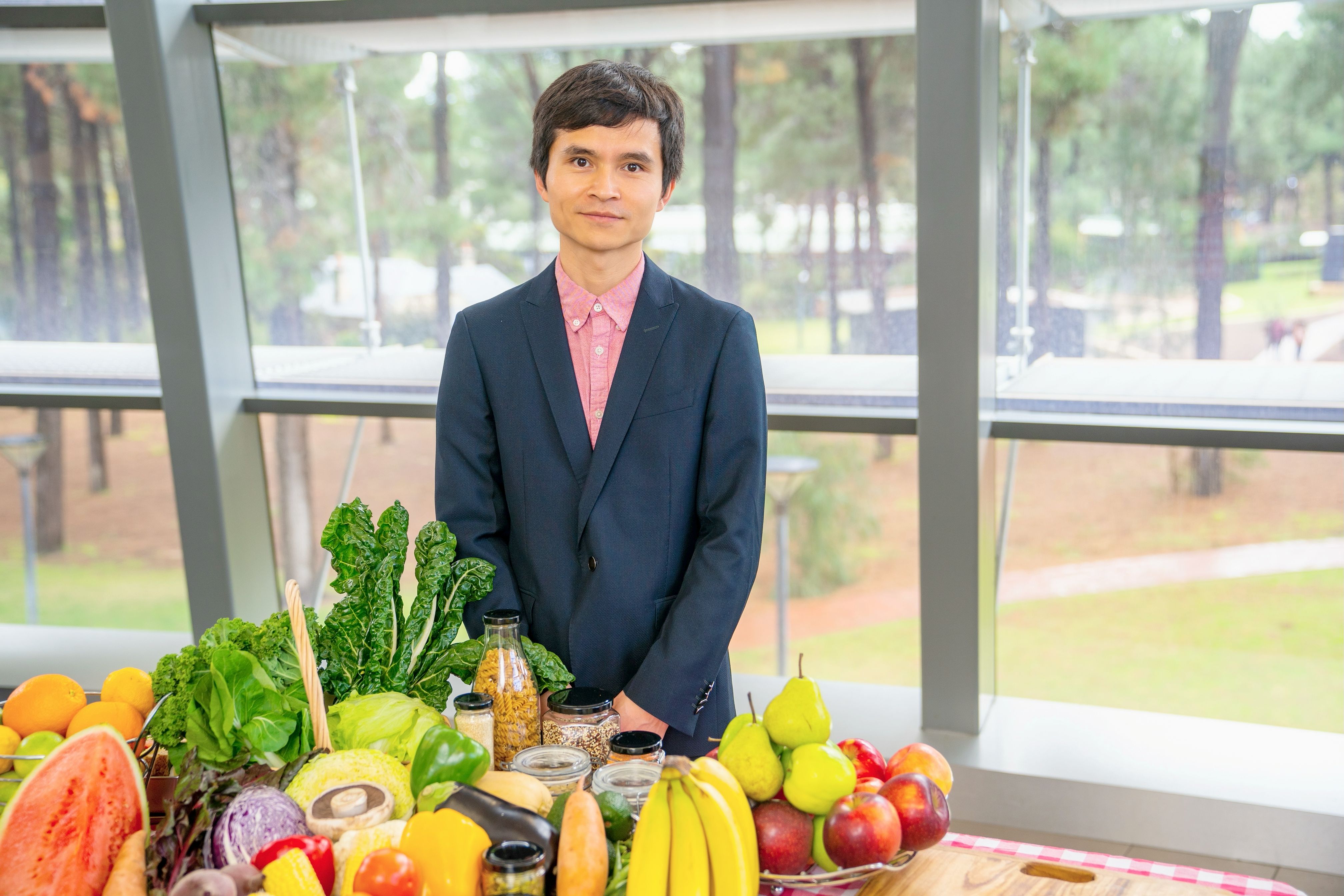 psa finalist liezhou zhong standing behind a collection of fresh fruits and vegetables 