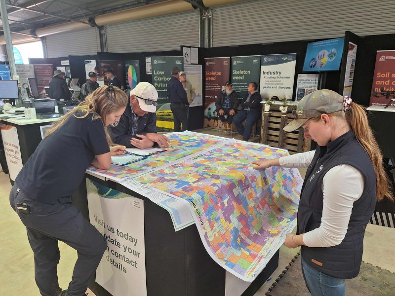 Three people looking at a property map on a table, with information display panels in the background.