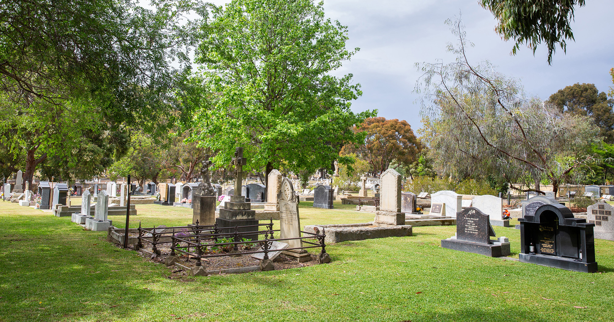 Old and new headstones sit side by side in a cemetery with green lawns and trees