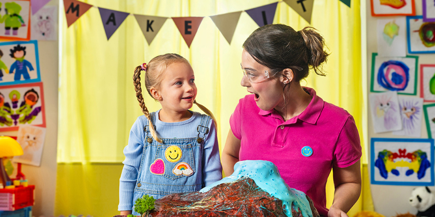 a little girl looking at a day care worker. A play volcano is in front of them