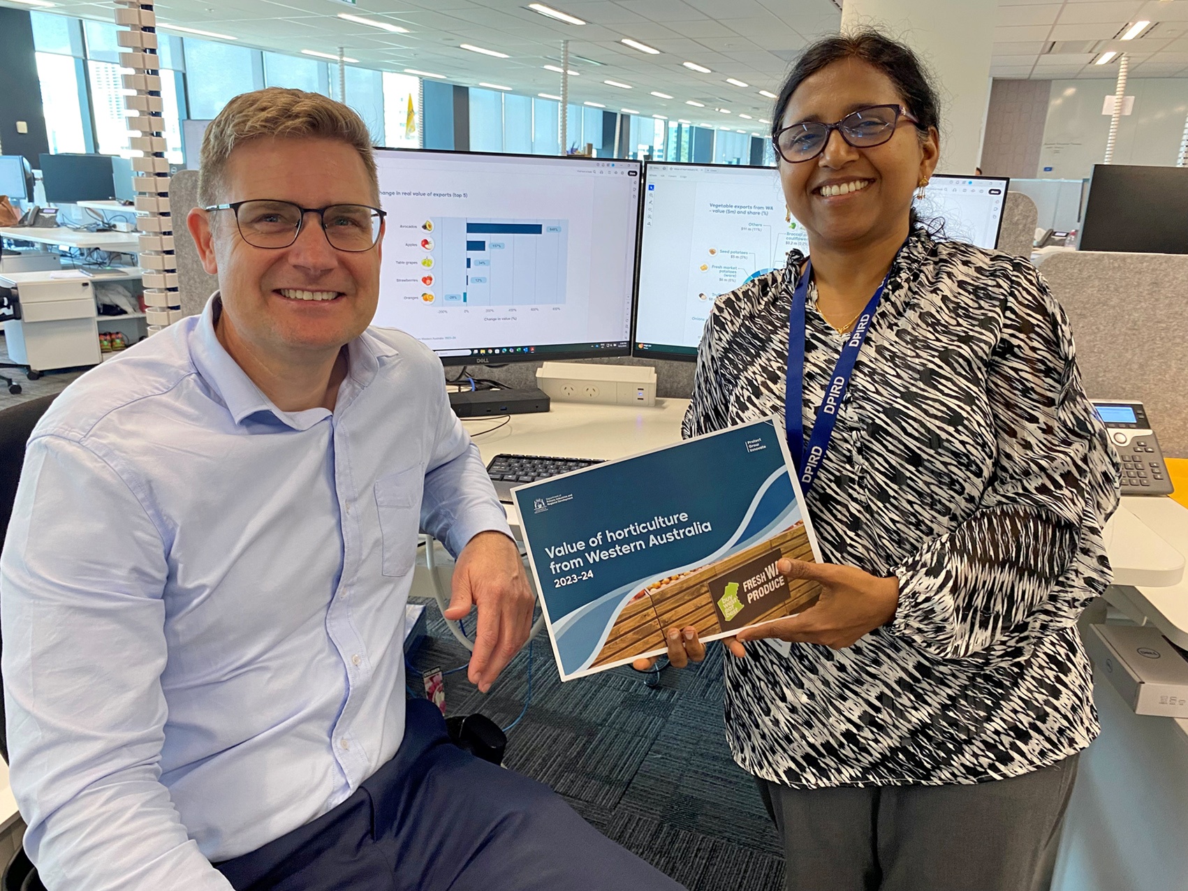 A man and a woman holding a book in an office.