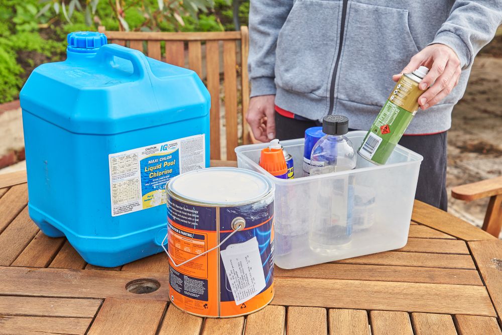 A collection of Household Hazardous Waste on an outdoor table, including a paint tin, chlorine container and aerosol cans.