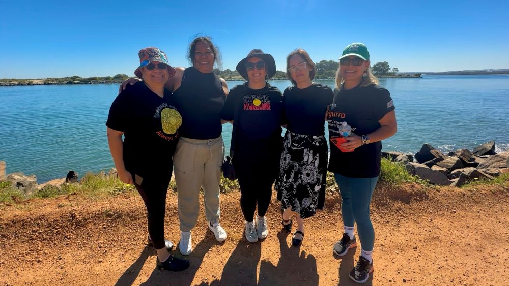5 women standing in front of a body of water