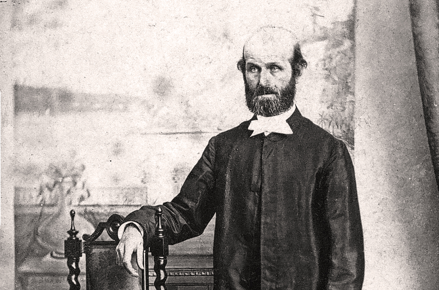 And old photo of a bald and bearded man wearing a plain dark suit with a white religious collar.