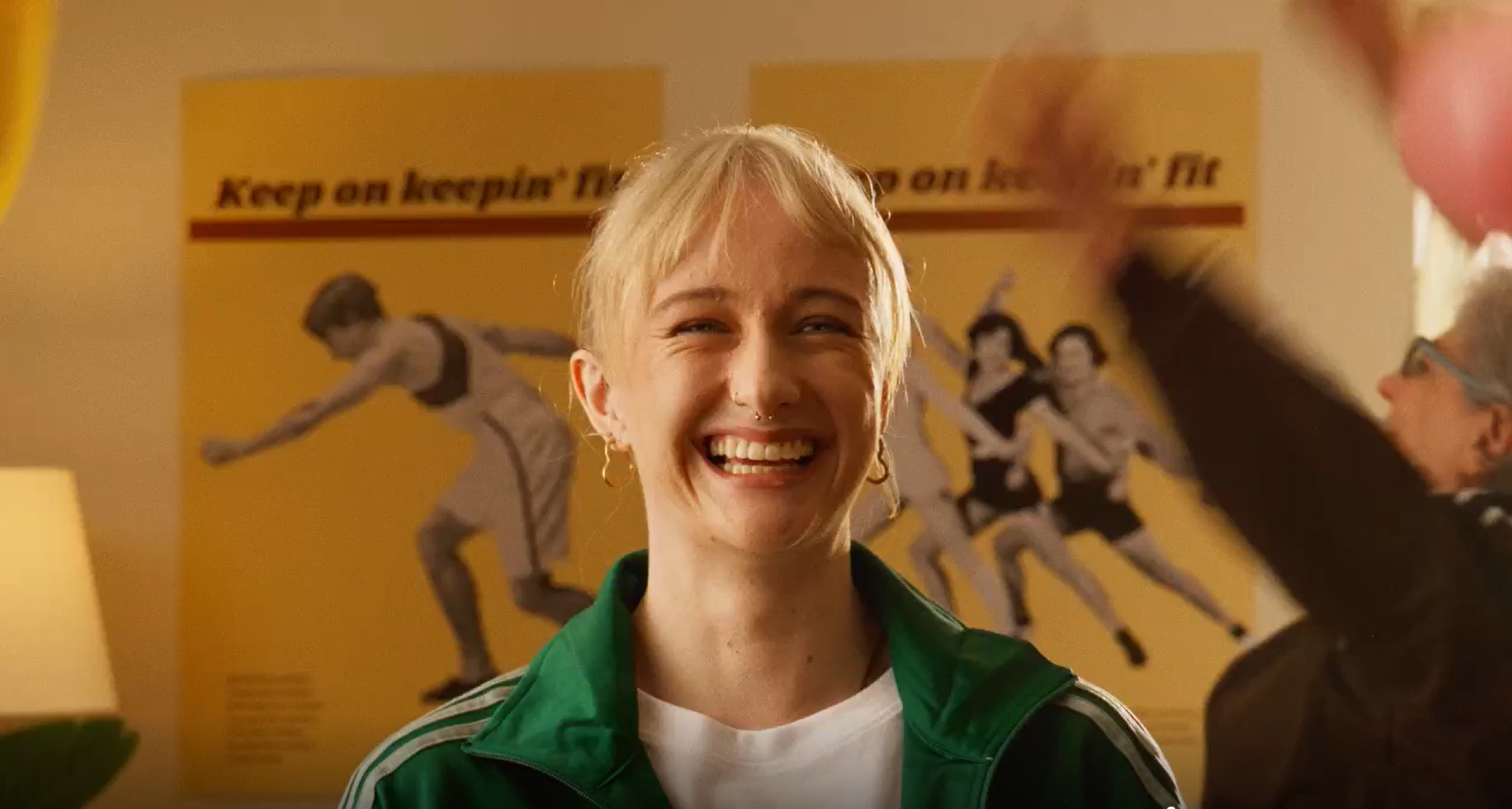 female facing the camera smiling with female in the background and posters on the wall