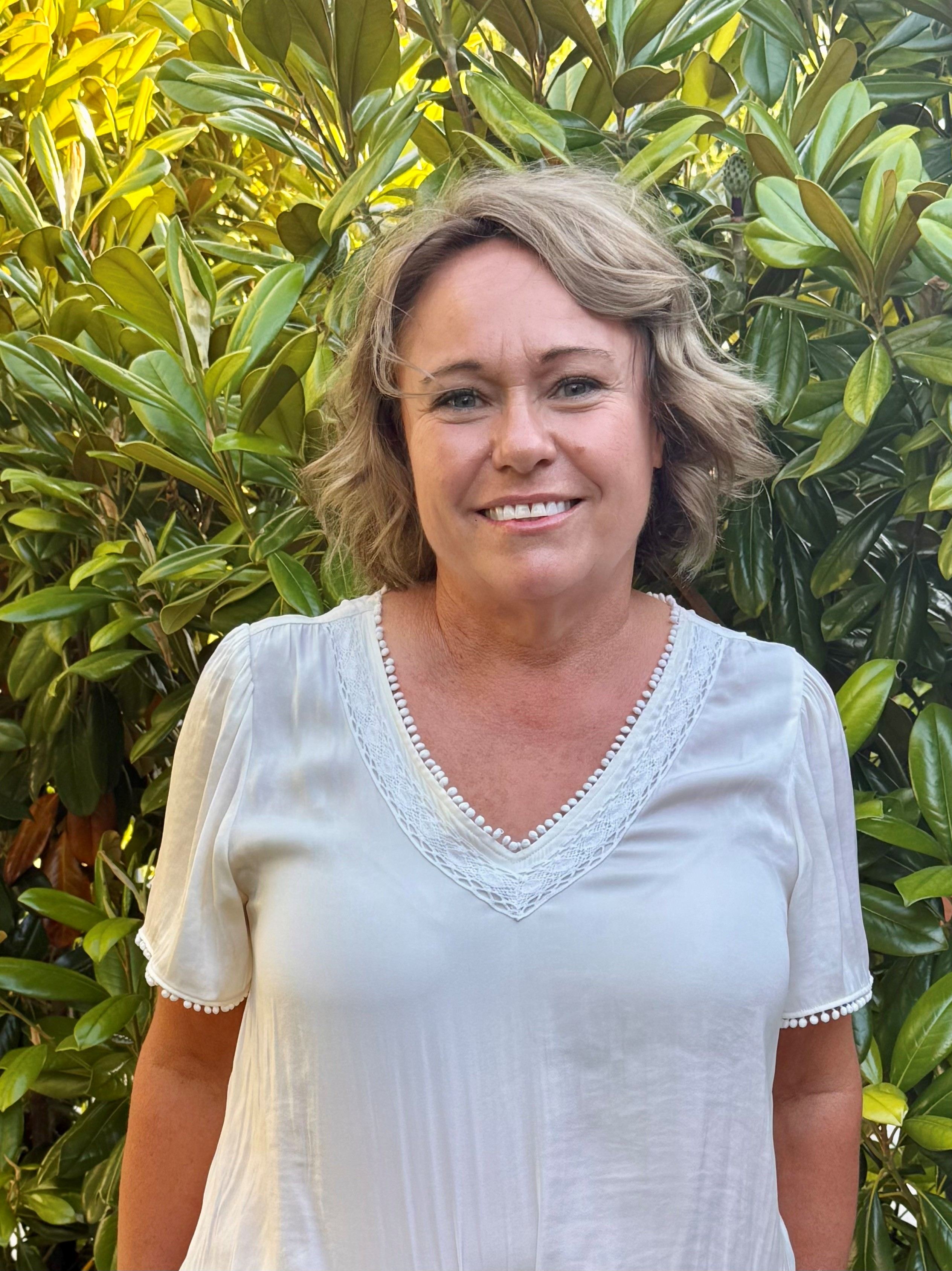 A headshot of a woman in front of a shrub.