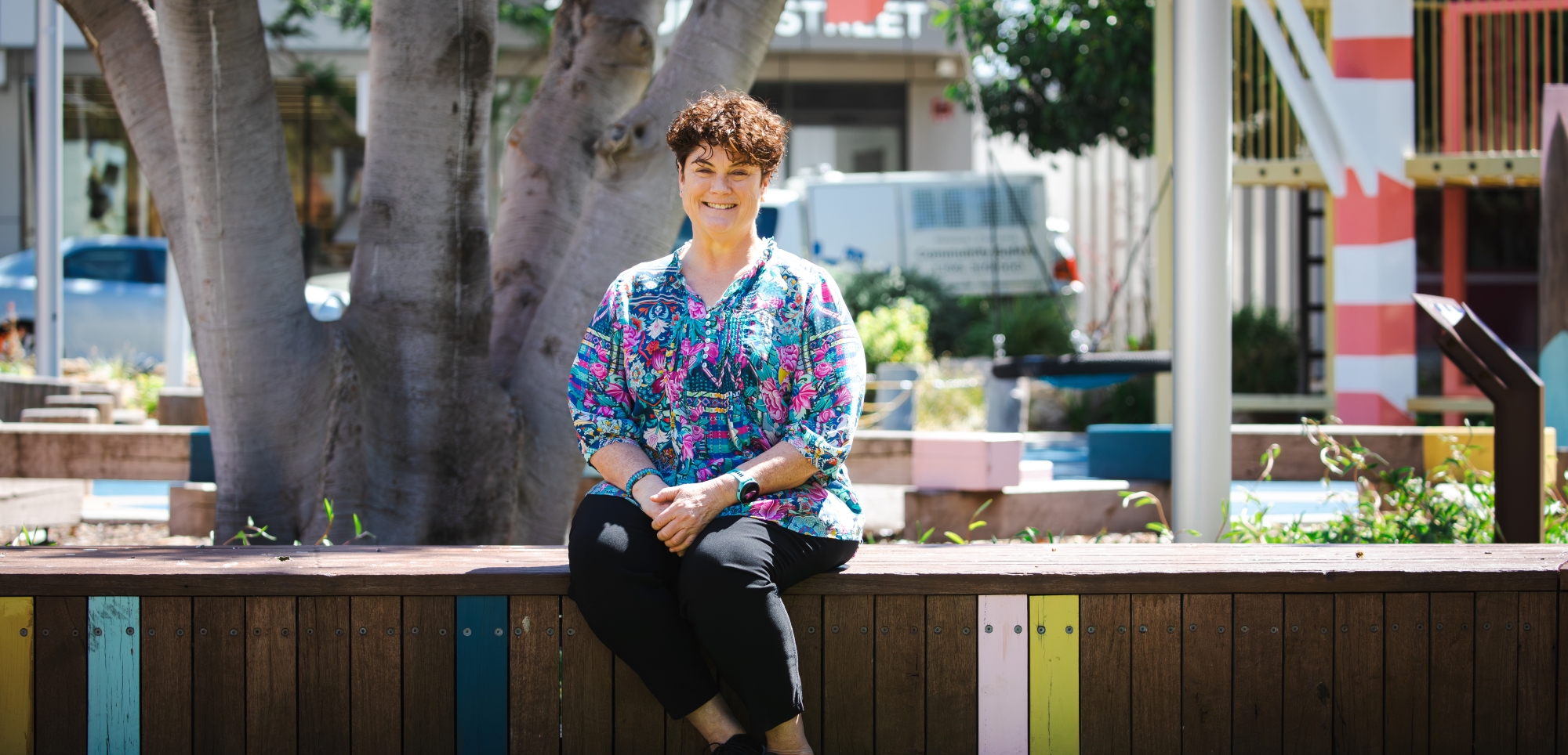 a middle age woman sitting on a park bench, smiling