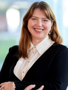 a woman wearing business attire, arms folded, smiling