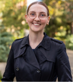 a well dressed woman, smiling, wearing glasses, pictured in an outdoor setting