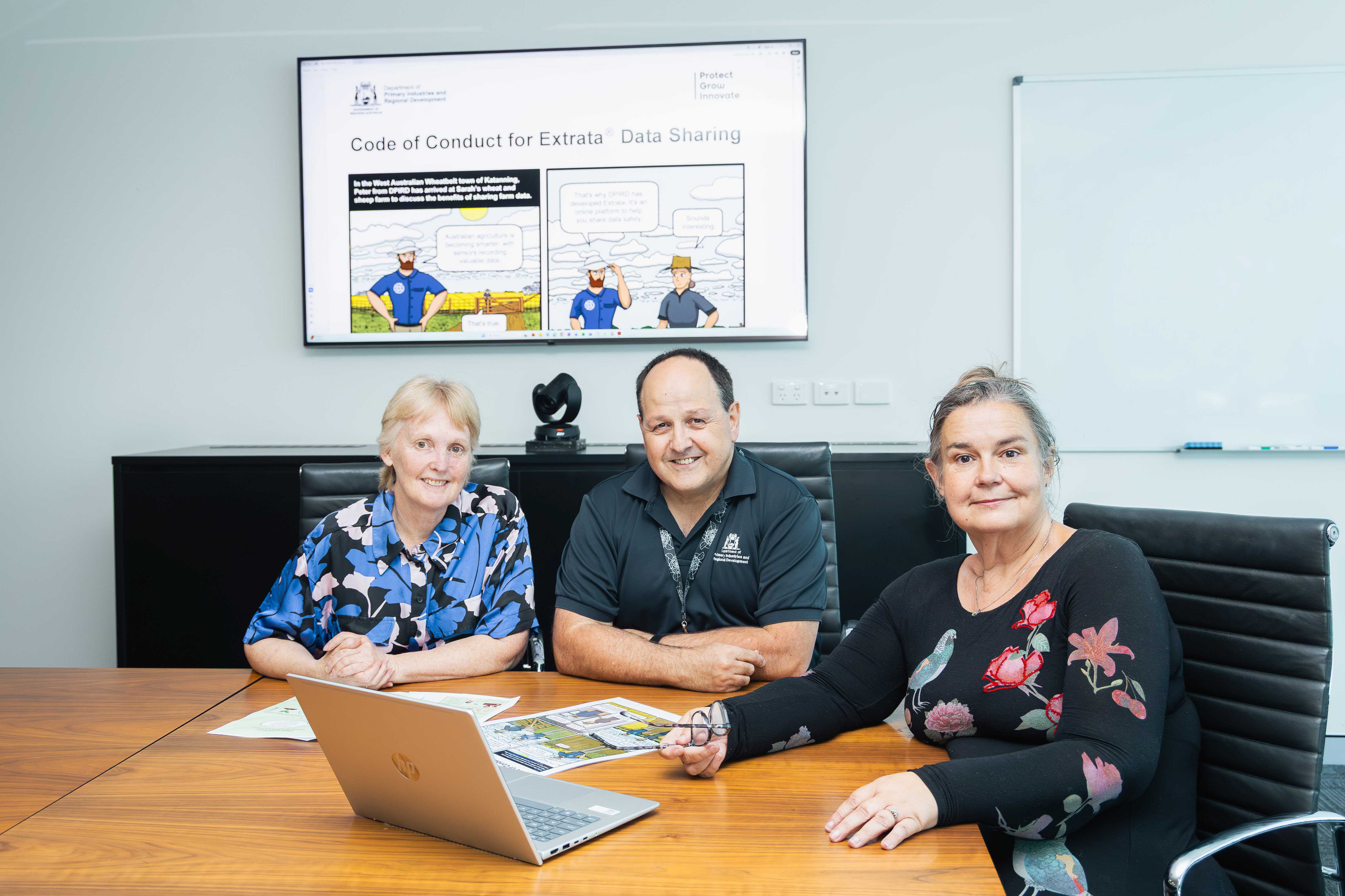 A man and two women in front of a big screen showing comic characters.
