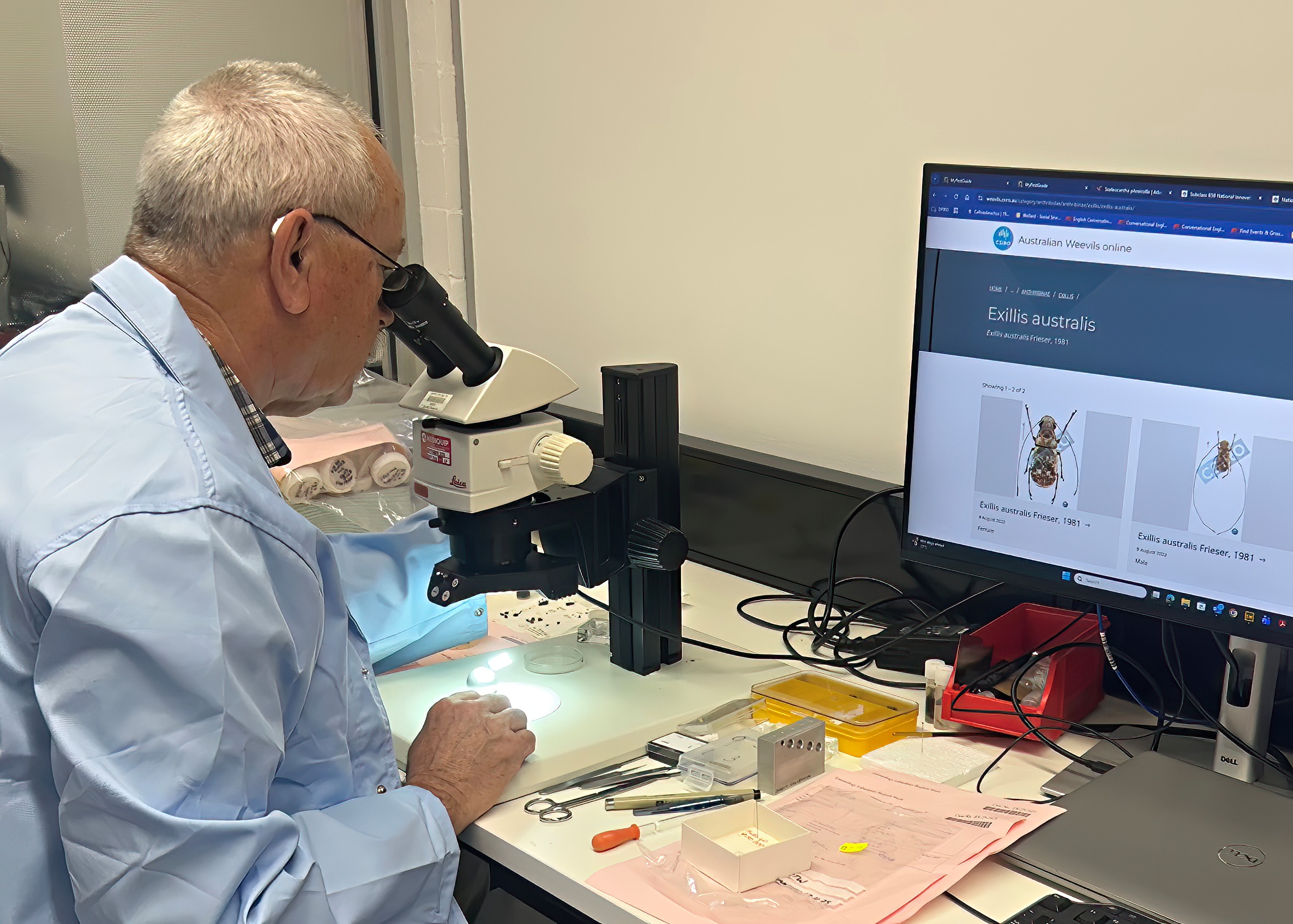 A man looking in a microscope in front of a computer screen.