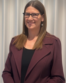 a woman with long brown hair, smiling, wearing glasses, wearing business attire
